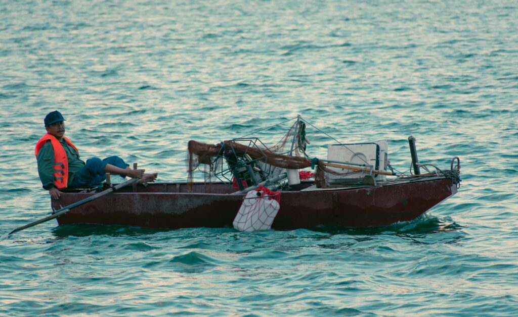 Mature fisherman wearing life jacket fishing with nets on a rowboat.